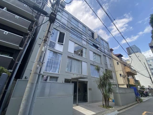 - モダンな外観のマンション、周囲に電柱と電線があり、晴れた空の下で撮影された都市の風景