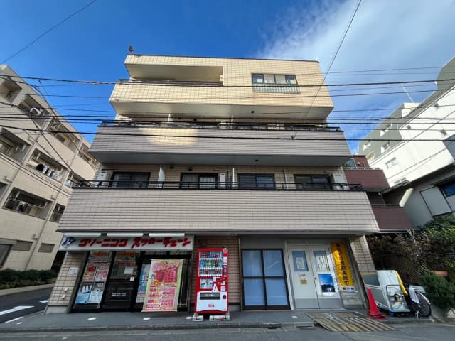 - 近代的な外観のアパートメントビル、1階にはクリーニング屋と自動販売機、青空が広がる都市の風景