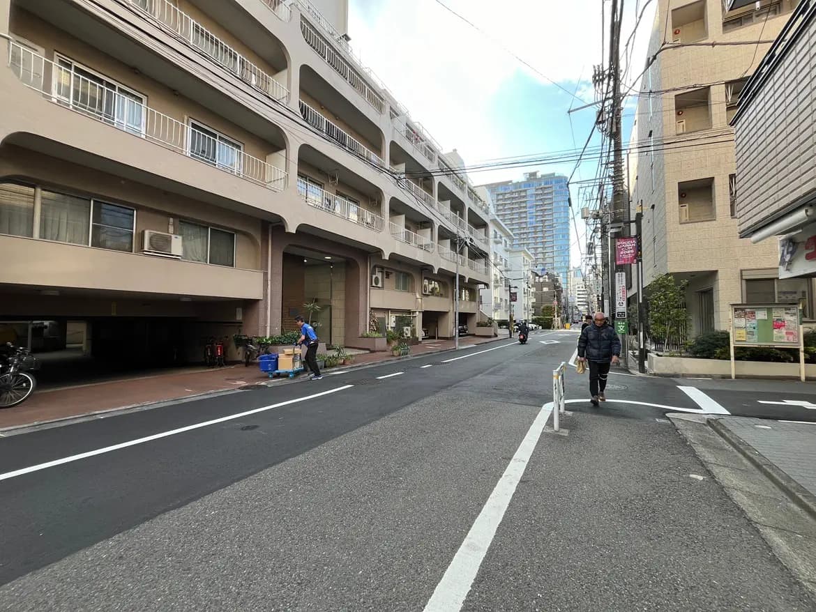 - 都市の景観が広がる街路、アパートメントビルと歩道に人が行き交う日常的な風景