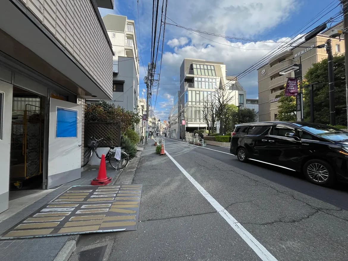 - 街中の風景、左側に自転車とさまざまな建物が並び、青空と雲が広がる静かな通りの様子