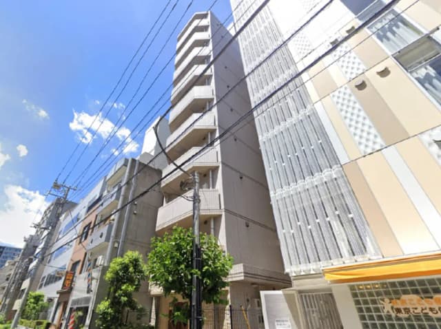 - 明るい空の下に立つモダンなアパートメントビル、周囲に緑豊かな木々と電柱が並ぶ都市風景