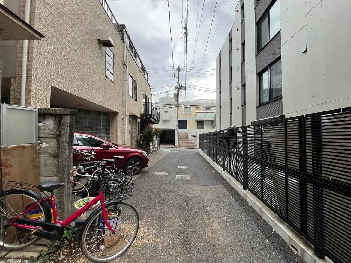 - 狭い街道に停まった自転車と赤い車、両側に立ち並ぶモダンな建物の風景
