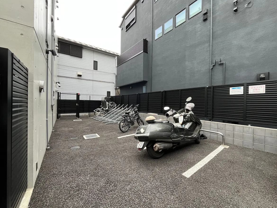 - 駐輪場の一角にあるバイクと自転車の停め方、周囲の黒いフェンスとコンクリートの壁が特徴的なエリア