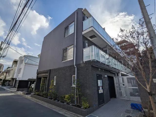 - モダンな外観の3階建てアパート、黒いタイルの壁とガラスのバルコニー、青空を背景にした街並み
