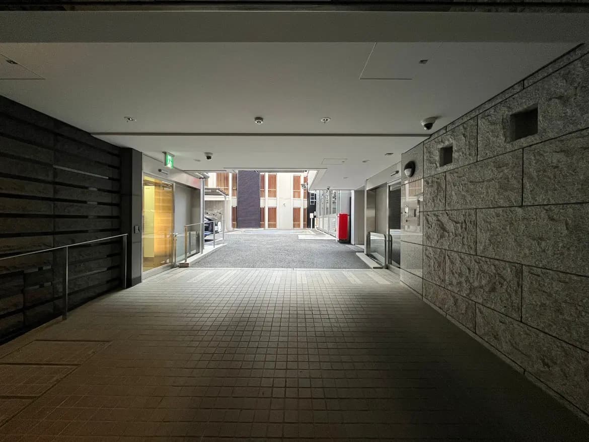 - 都市のアーケード、モダンな建築と照明、左側にガラスドアと手すり、背後に見える車道の風景
