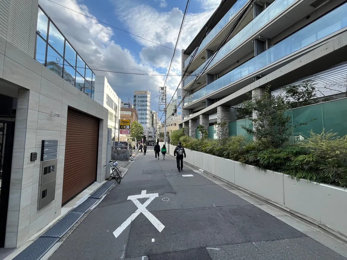 - 都市の歩道と近代的な建物、青空と雲が広がる風景、通行人と自転車が見える街の風景