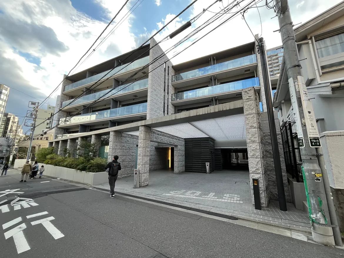 - モダンな外観のマンション、広いアプローチと駐車スペース、周囲に高層ビルが立ち並ぶ街並み