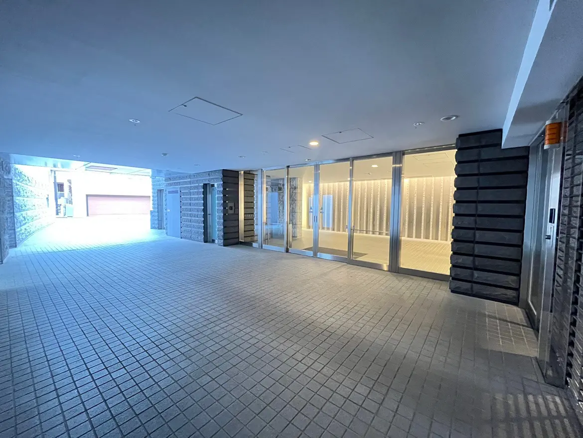- 明るい照明が照らす広々としたエントランス、モダンな外観の建物と石造りの壁が映えるエリア