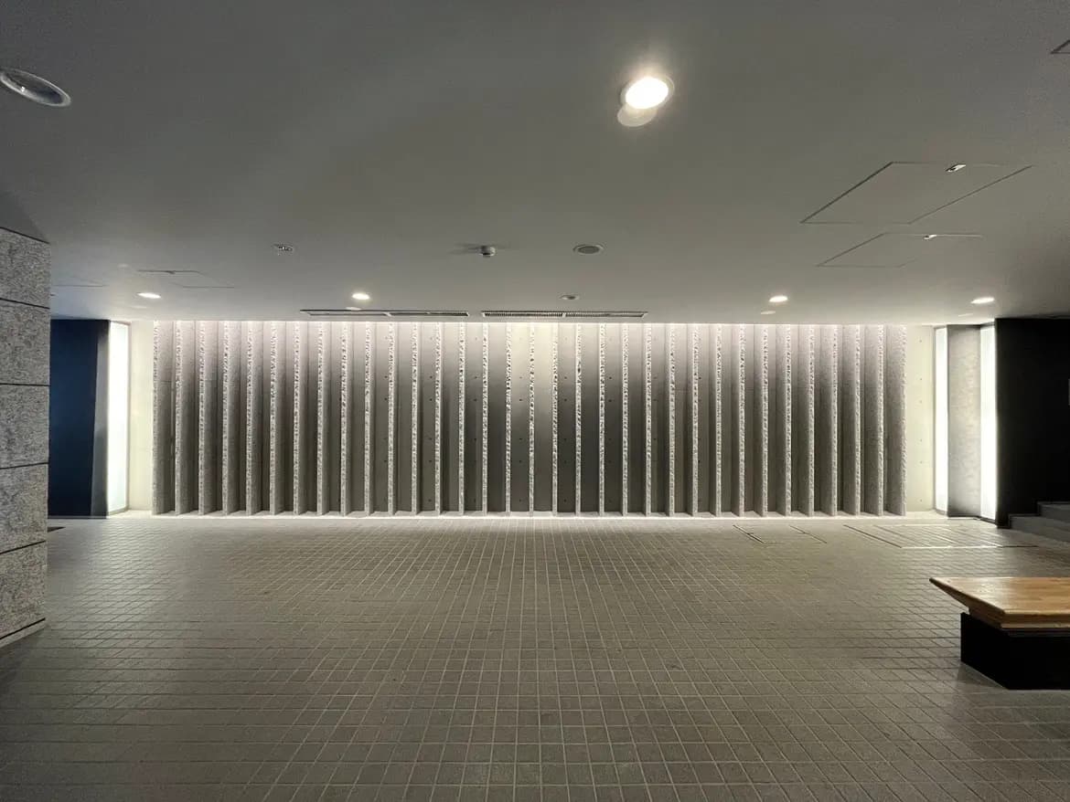 - モダンなデザインの空間、照明で際立つテクスチャーのある壁と整然とした床タイル、シンプルな家具が配置されたインテリア