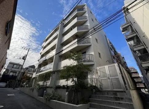 - 都市部に立地する現代的なマンション、明るい外観と植栽が配されたエントランス、青空が広がる背景