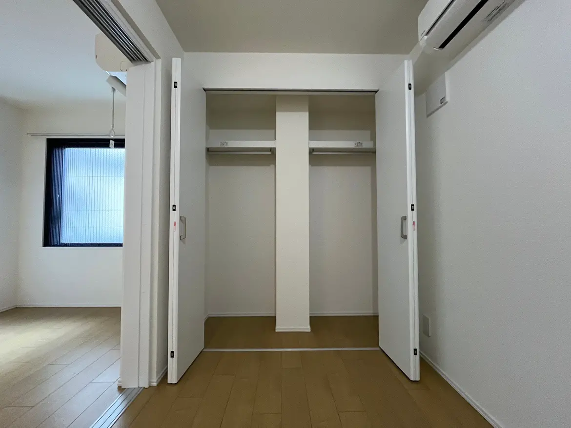 空白の壁とフローリングがある新築マンションの居間、白色のスライドドア、エアコン付き