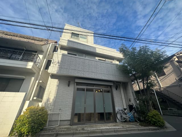 現代的なデザインの都市型一戸建て、白壁と大きな窓、青空と電線が交差する背景