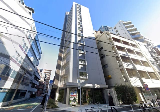 - 都市の中心に立つモダンな高層ビル、周囲の建物に囲まれた外観と青空が広がる街並み