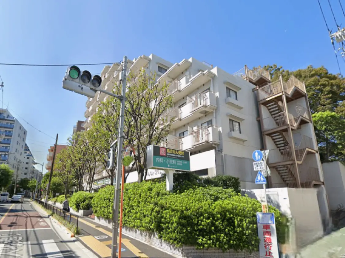 - 緑豊かな街並みと白いマンション、青空の下に立つ信号機と交通標識が映える風景