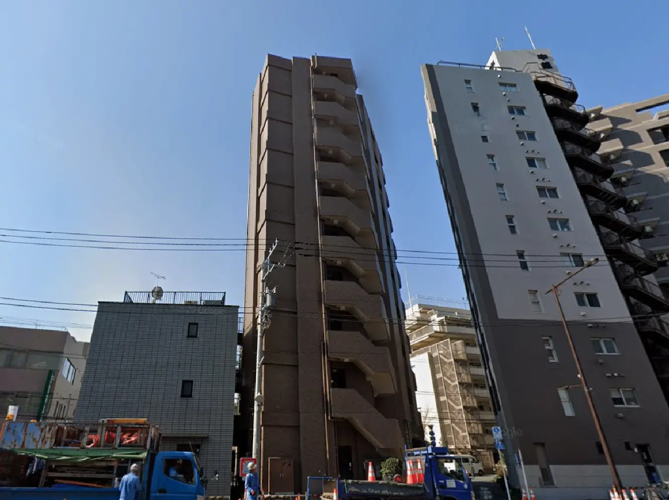 - 近代的なデザインの複数階建てのアパートメントビル、隣接する建物と青い空、道路工事中の様子が写る都市の風景