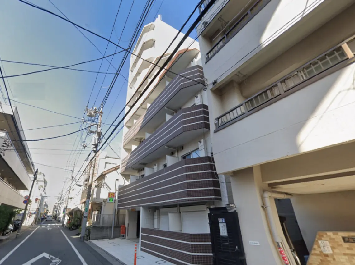 - 通りに面したアパートの外観、バルコニー付きのモダンな建物と青空、電線が見える都市の風景