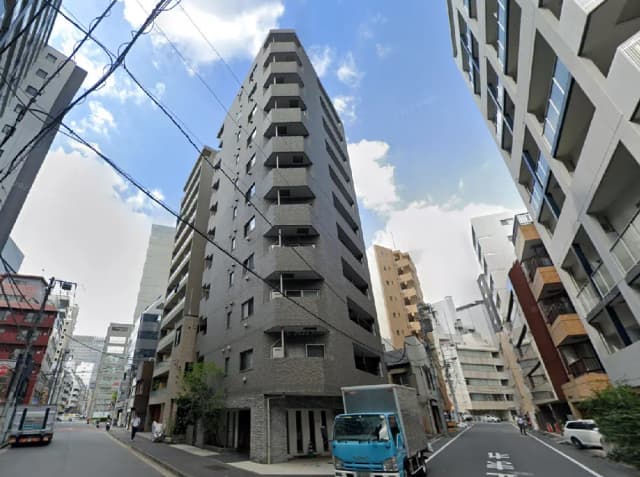 - 高層マンションの外観、灰色のタイル張り、近隣のビルとのコントラスト、青い空が広がる都市の風景