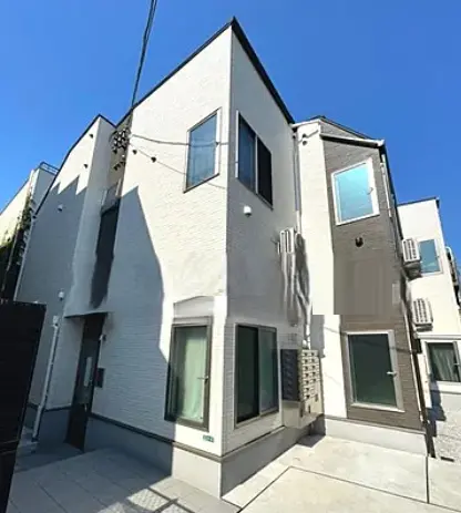 - 明るい日差しが差し込む外観の住宅、白い外壁と黒いアクセントが特徴的な3階建ての建物、窓が整然と配置されたモダンなデザイン
