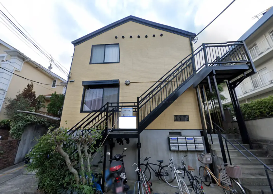 - 外階段のある黄色い外壁の住宅、周囲に自転車とバイクが停まっている様子