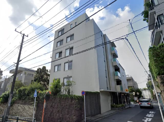 - モダンなアパートメントビルの外観、周囲には緑があり、晴れた空と電線が見える街並みの景色