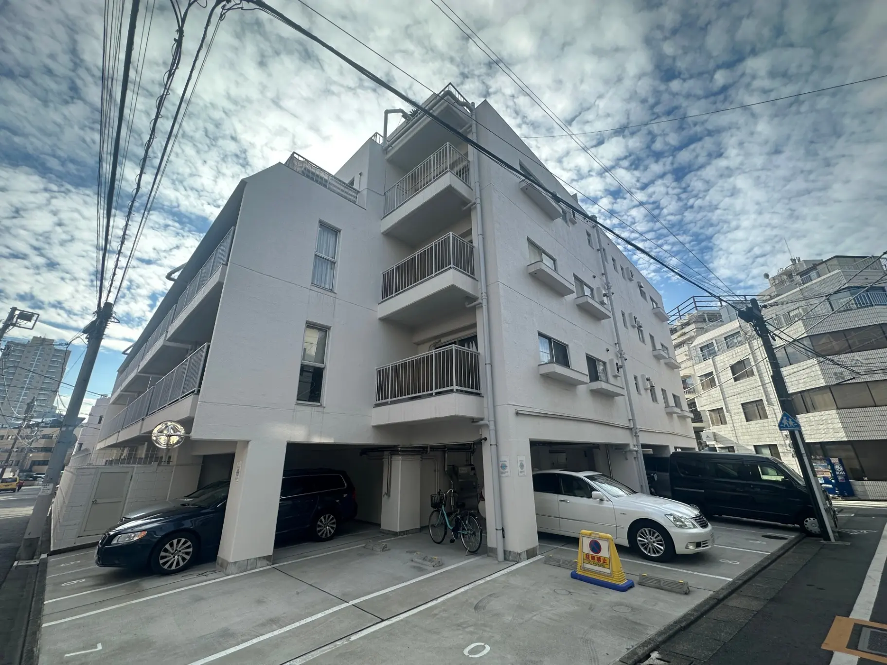 都市のマンション、白い外壁とバルコニー、地上階に駐車スペースがある建物