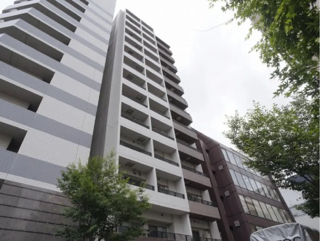 現代的なデザインの高層マンション、灰色の外壁とバルコニーが特徴、周囲に緑の木々が見える風景