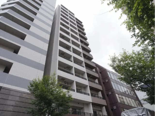 現代的なデザインの高層マンション、灰色の外壁とバルコニーが特徴、周囲に緑の木々が見える風景
