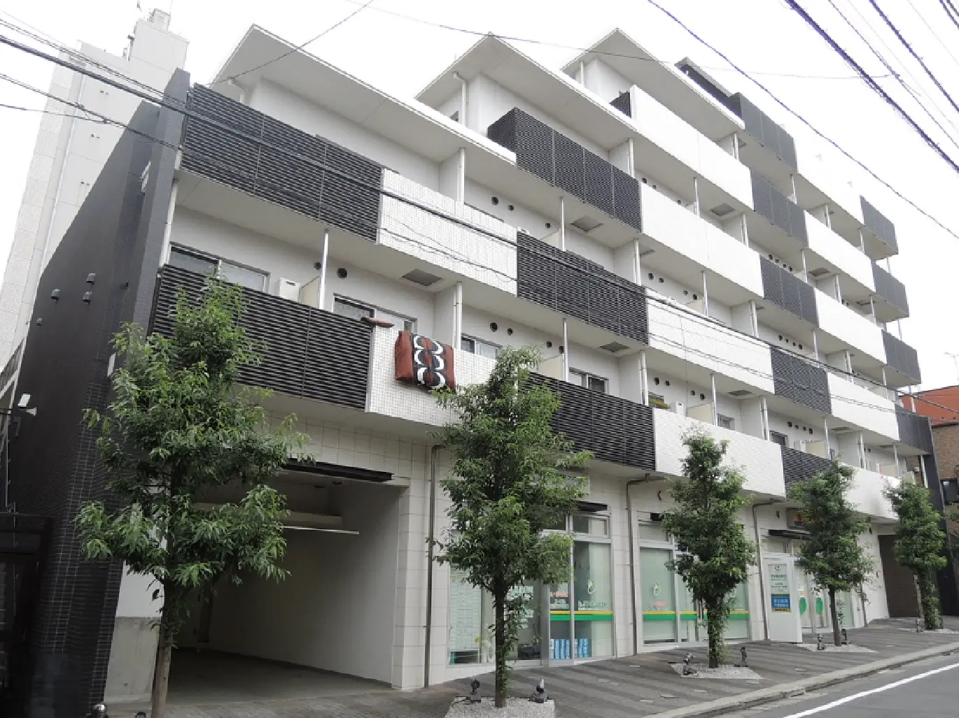 - モダンなデザインのアパート外観、白と黒のコントラスト、バルコニーに植栽が施された都市型住宅