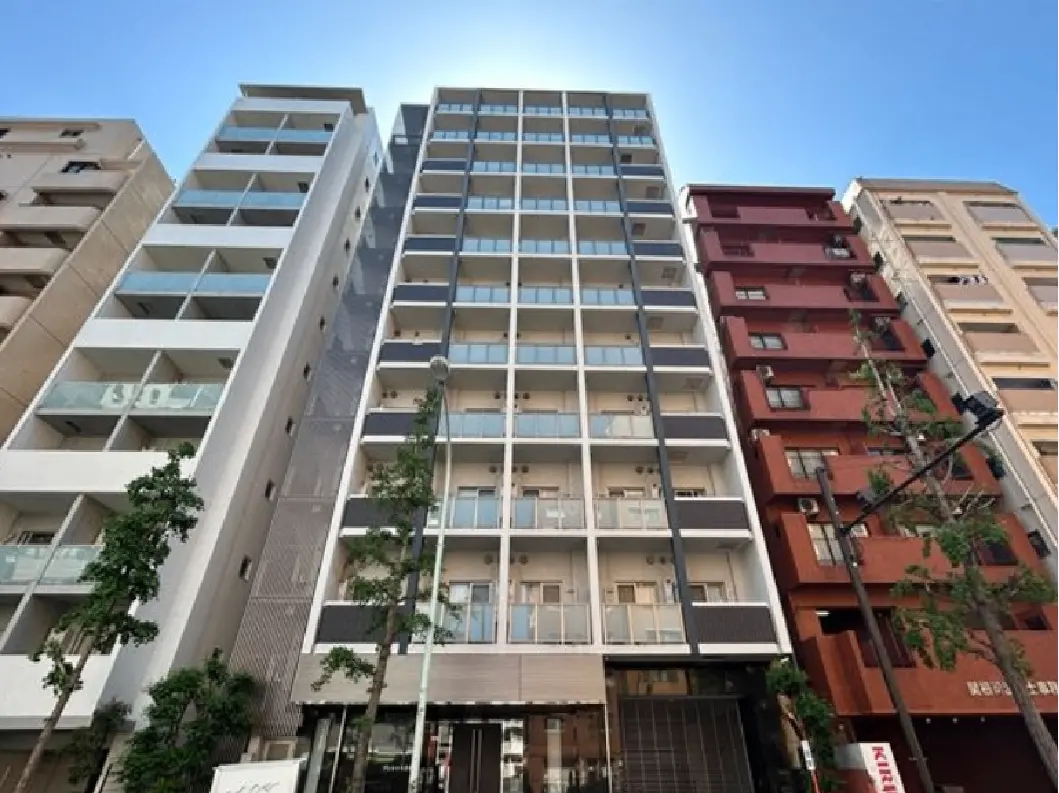 - モダンなデザインの高層マンション、隣接する住宅とバルコニーが施された外観、青空が背景の街並み