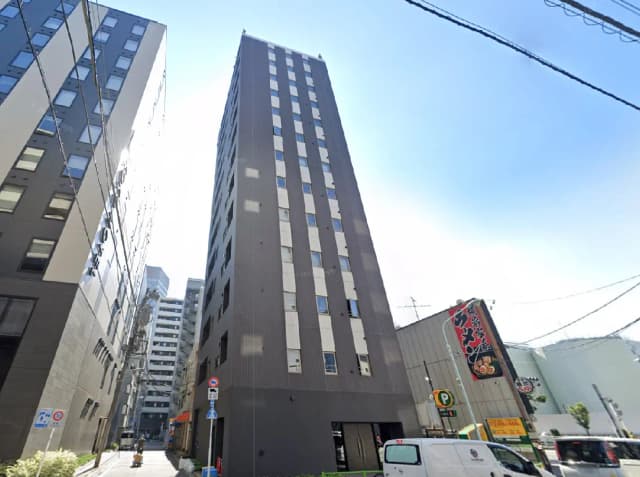 - 高層ビルが並ぶ街並み、シンプルなデザインの建物と晴れた青空、周囲には飲食店や駐車場が見える風景