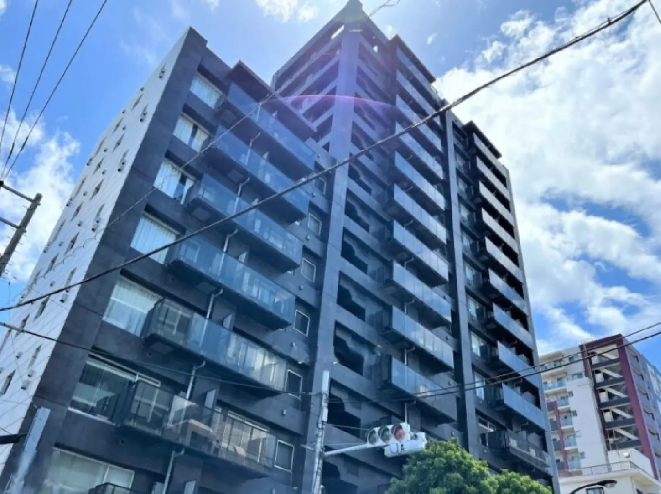 - 黒い外壁の現代的なマンション、バルコニーと大きな窓が特徴、青空と雲が映える高層建築の風景