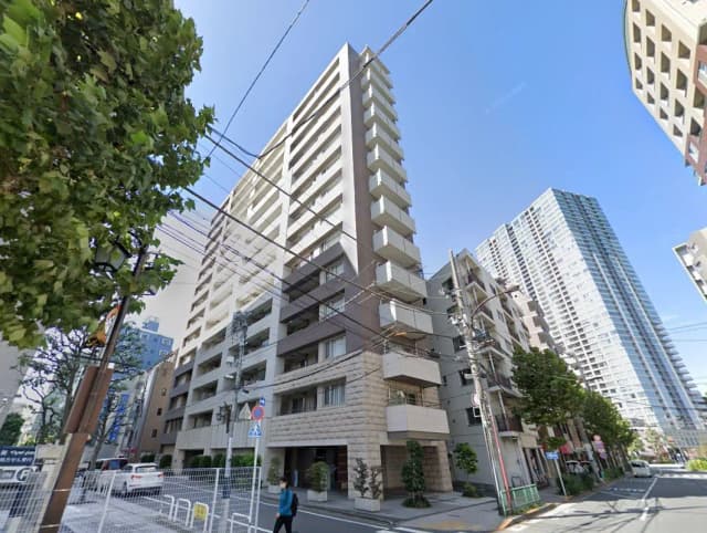 都市の住宅街にあるマンション、晴れた日の青空、周囲には高層ビルと街路樹