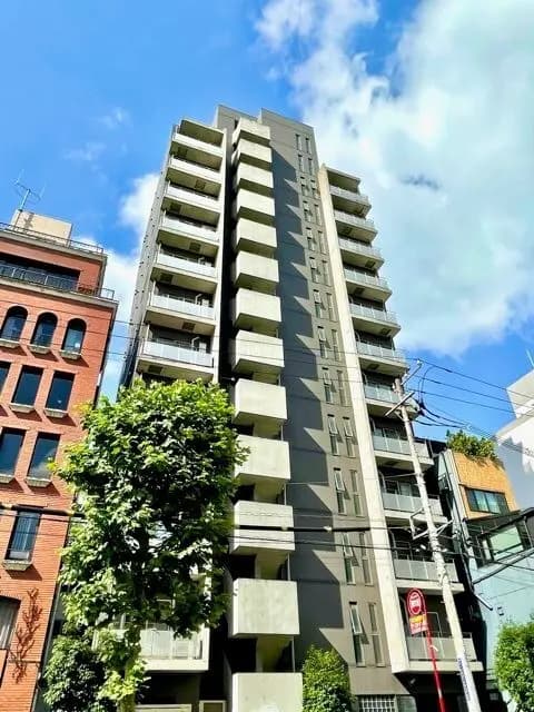 - 現代的なデザインの高層マンション、青空の下で太陽光を浴びる外観、緑の木々が印象的な都市の風景