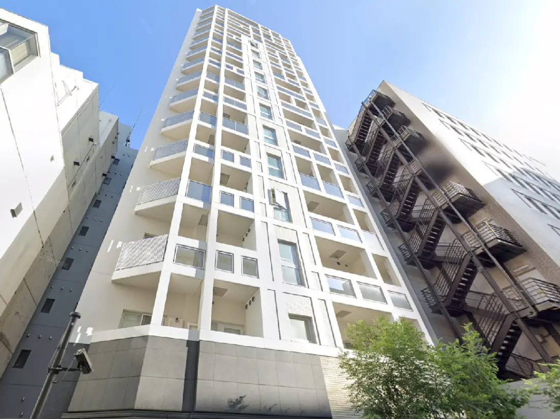 - モダンなマンションの外観、白い外壁とバルコニー、大きな窓が特徴、隣接する建物と青空の景観