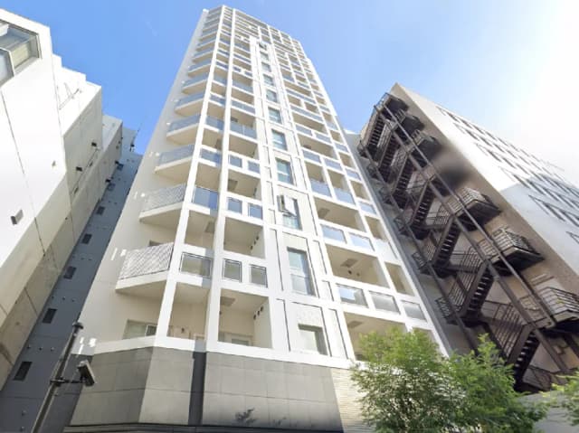 - モダンなマンションの外観、白い外壁とバルコニー、大きな窓が特徴、隣接する建物と青空の景観
