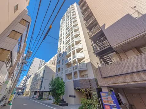 - 青空の下、現代的なデザインの高層マンションと周囲の建物が立ち並ぶ通りの風景