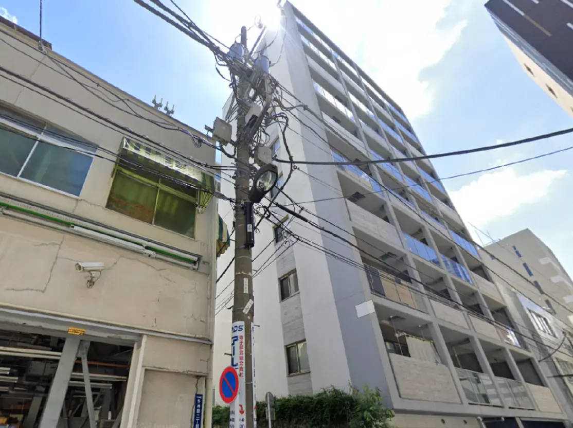 - 高層マンションの外観、電柱と電線が交差し、青空と太陽が映える街の風景