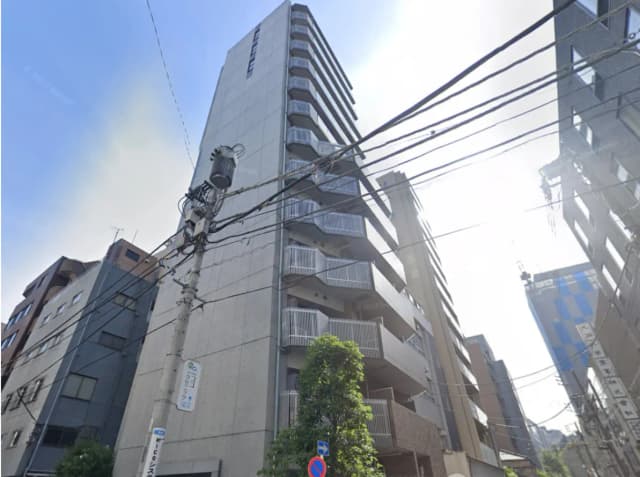 - 高層マンションの外観、コンクリートの壁とバルコニー、周囲の建物や電線が見える都市の風景