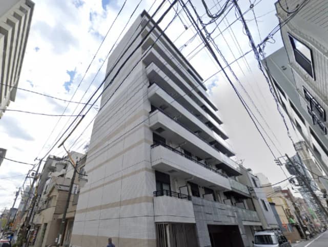 - 近代的な外観のマンション、白いタイル張りのファサード、複数のバルコニーと周囲の建物が見える街並み