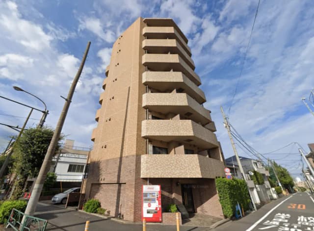 - 都市型のスタイリッシュなマンション外観、バルコニーとブラウンのタイル張り、青空の背景