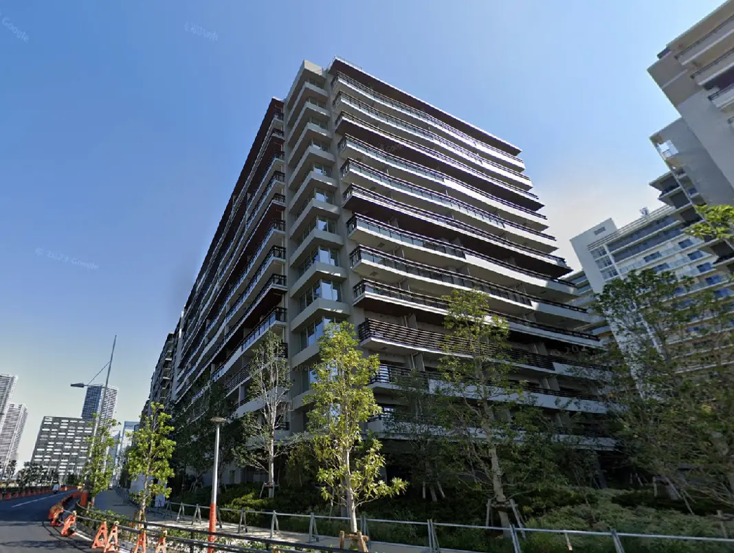 現代的なデザインの高層マンション、緑豊かな植栽と青空が映える外観、整備された歩道と周囲の都市景観