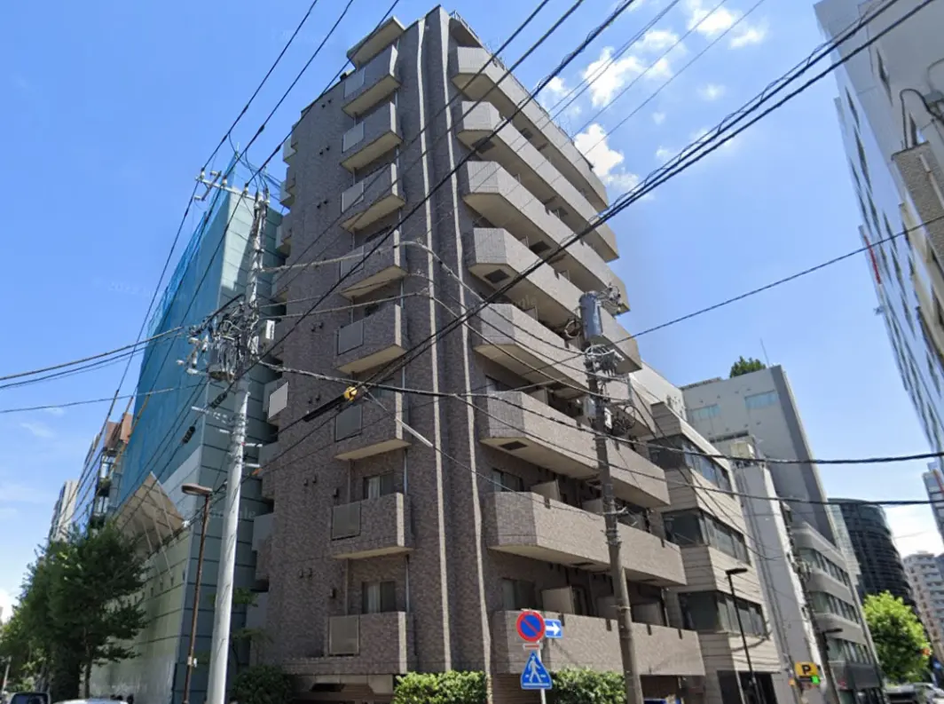 - 都市の風景に立つモダンなマンション、周囲には電線が張り巡らされ、青空が広がる様子