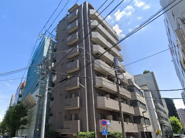 - 都市の風景に立つモダンなマンション、周囲には電線が張り巡らされ、青空が広がる様子
