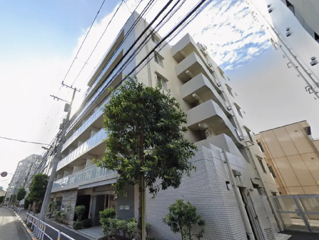- モダンなデザインのマンション外観、青空と電線が写る都市風景、緑の植栽が周囲を彩る