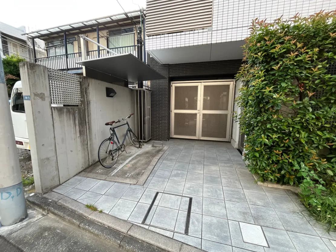 - 自転車が置かれたモダンなエントランス、タイル張りの床と周囲の緑に囲まれた入口の風景