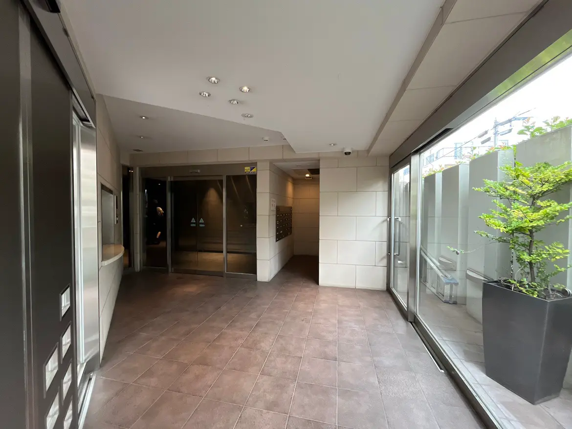 - モダンなエントランスホール、ガラスのドアと緑の観葉植物が配置された広々とした空間、明るい照明とタイルの床が特徴