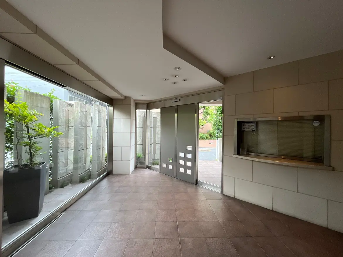 - モダンなエントランスホール、ガラスの窓からの自然光とシンプルなデザインの壁、観葉植物が配置されたスペース