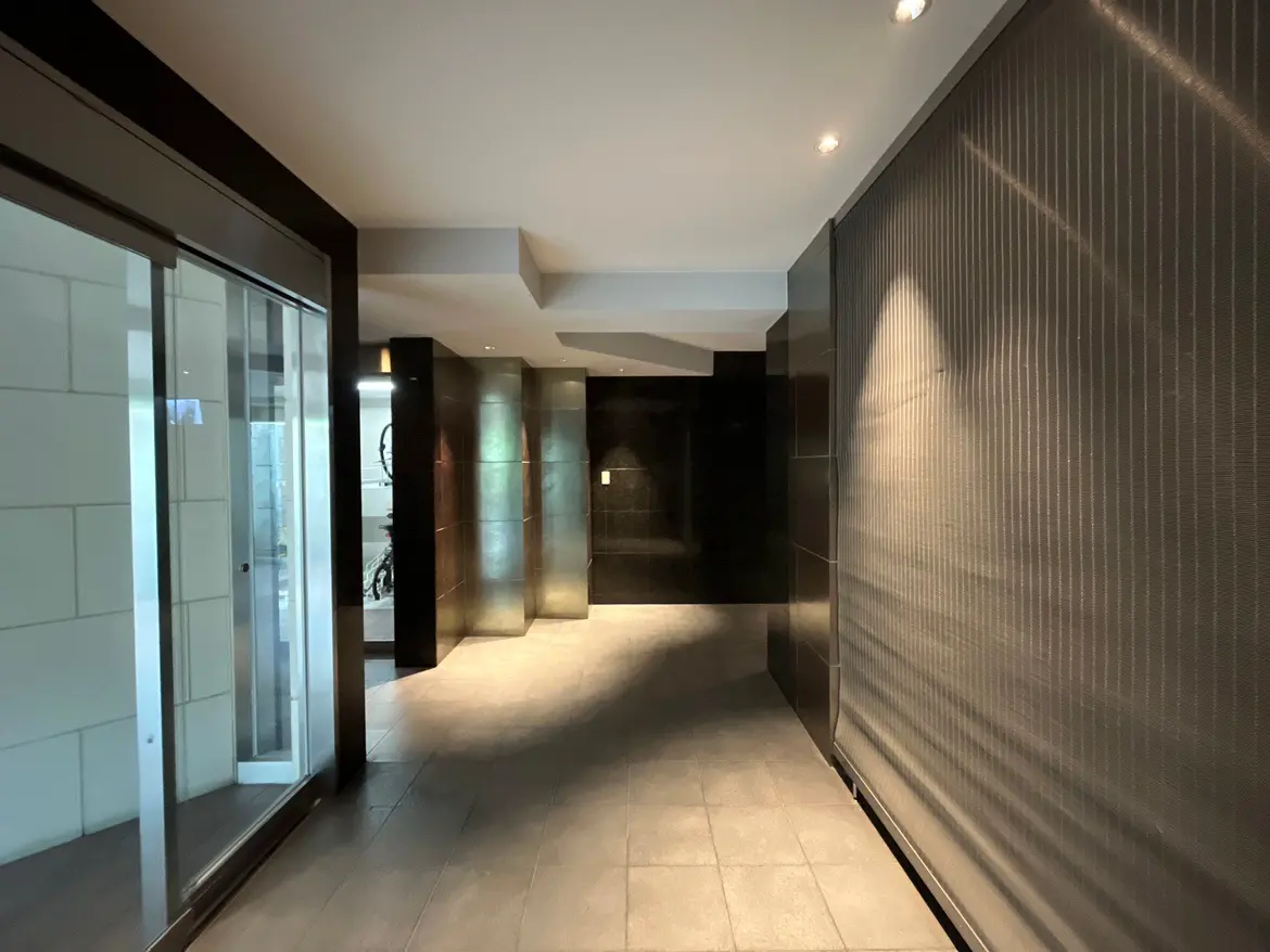 - モダンなデザインのエントランスホール、シンプルなタイルの床、照明が施された壁、ガラスドアが見える空間