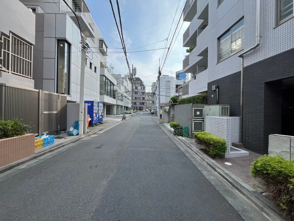 - 都会の静かな通り、近代的な建物と整備された緑地、遠くに見える高層ビルと青空が映える風景