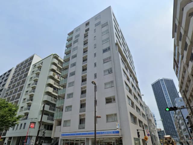 - 白い外観の高層マンションと隣接するビル群、下にはコンビニと信号機がある都市景観